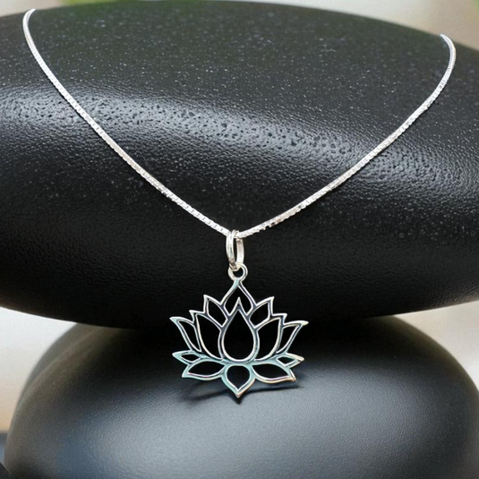 Silver lotus flower necklace on a black stone with greenery in the background