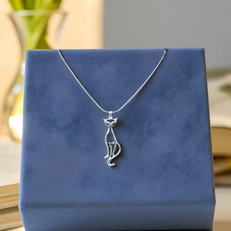 Load image into Gallery viewer, Silver necklace with a pendant on a blue jewelry box, with orange flowers in the background.
