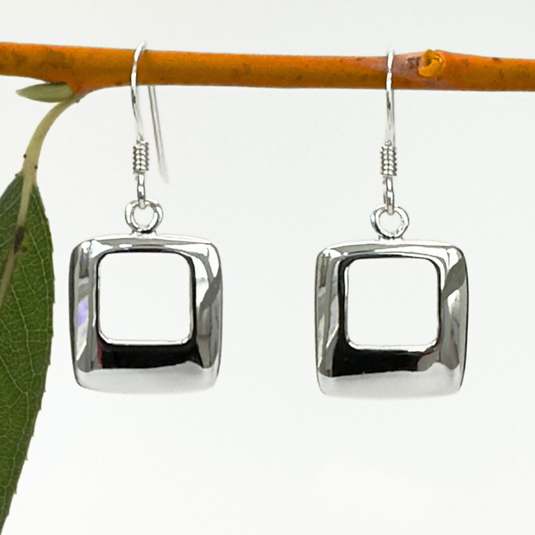 Silver square earrings hanging from a branch with leaves.