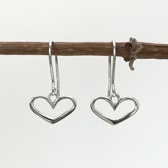 Heart-shaped silver earrings hanging from a branch on a white background