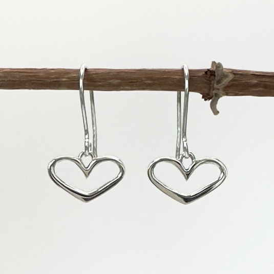 Heart-shaped silver earrings hanging from a branch on a white background