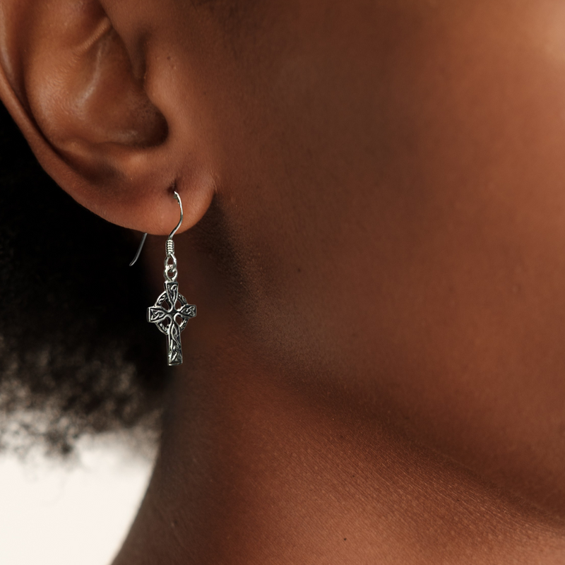 Load image into Gallery viewer, Close-up of an ear wearing a silver cross earring with a blurred background
