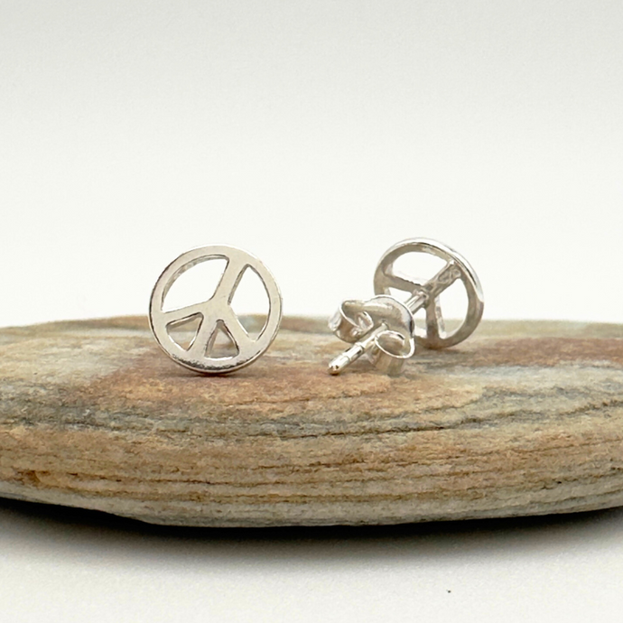 Silver peace sign earrings on a wooden surface with a white background