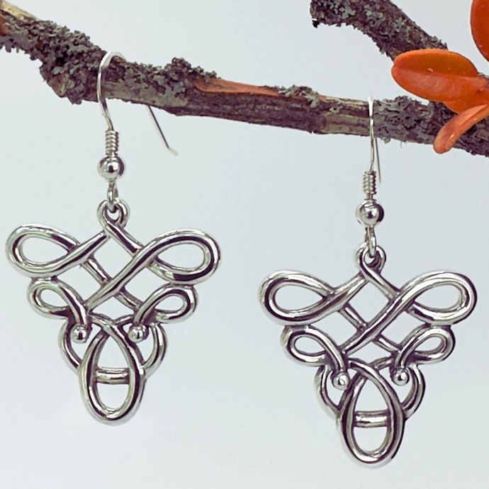 Silver Celtic knot earrings on a branch with a white background