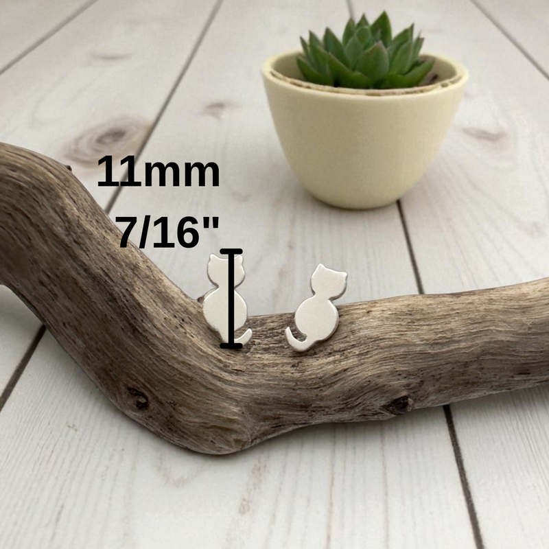 Load image into Gallery viewer, Small white cat-shaped earring on a wooden branch with measurement text and a potted plant in the background.
