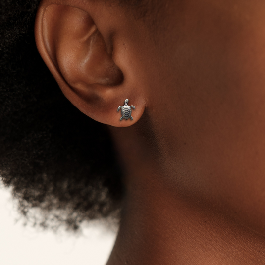 Close-up of an ear wearing a turtle-shaped earring with a blurred background