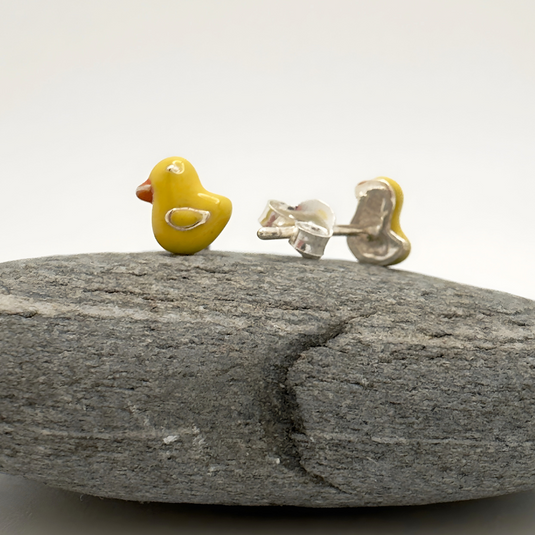 Yellow rubber duck and silver earring on a gray stone with a white background