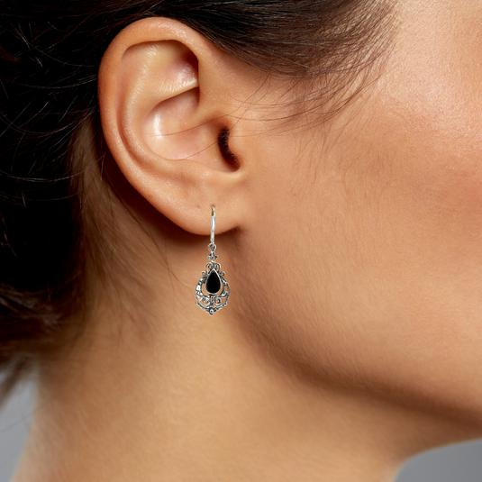 Close-up of a person wearing a black teardrop earring with a gray background