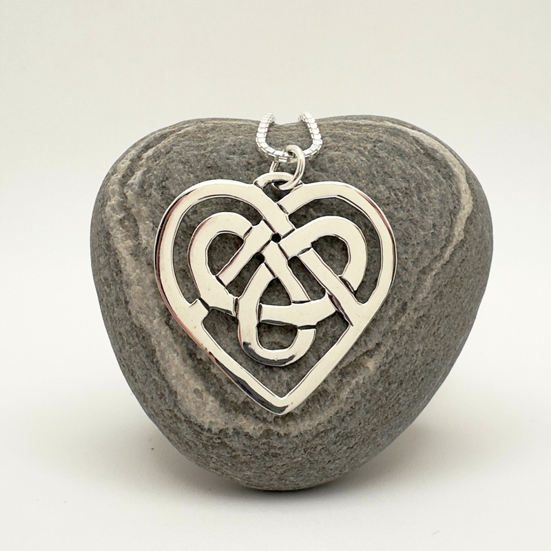 Load image into Gallery viewer, Silver Celtic knot heart pendant on a stone background
