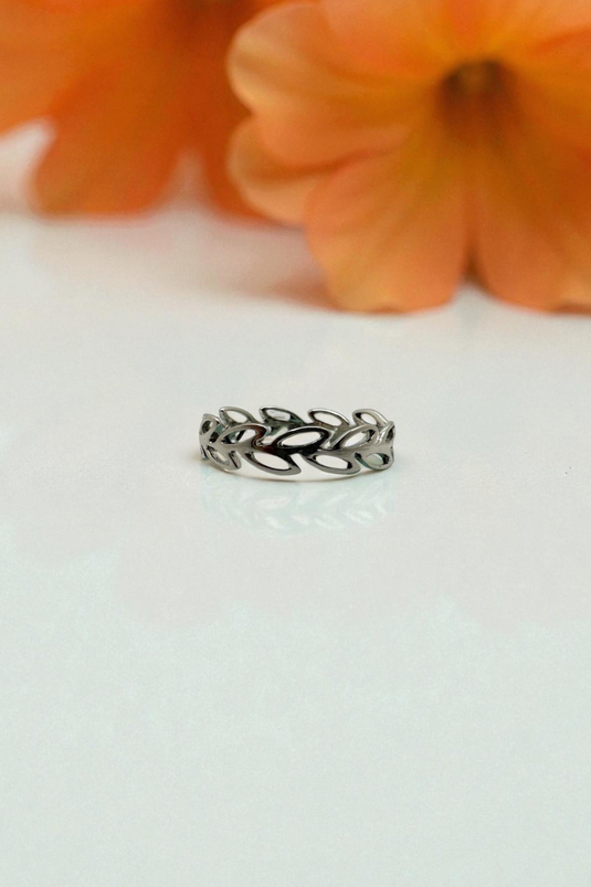 Silver ring with leaf design on a white surface with orange flowers in the background