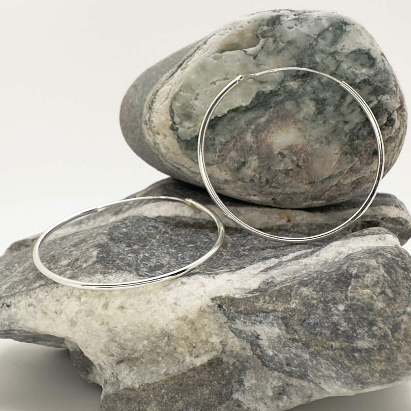 Load image into Gallery viewer, Silver hoop earrings on a stack of gray stones with a white background
