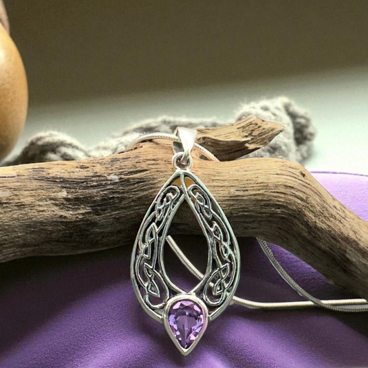 Silver pendant with a purple gemstone on a wooden branch and purple fabric background