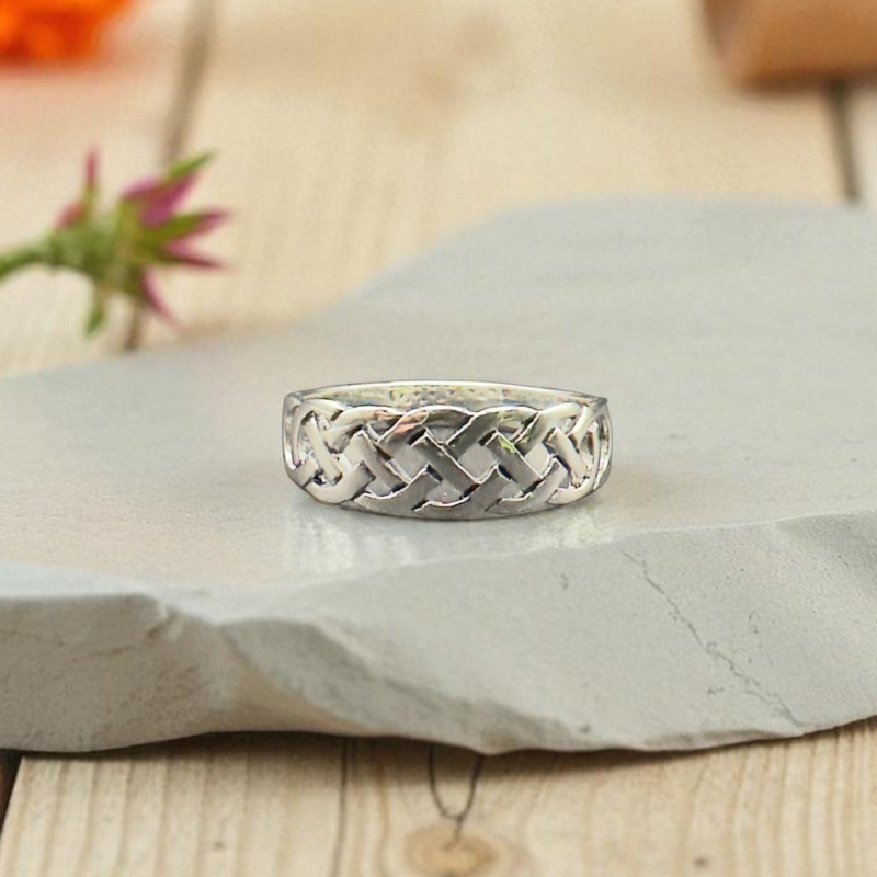 Load image into Gallery viewer, Silver braided ring on a stone surface with flowers in the background
