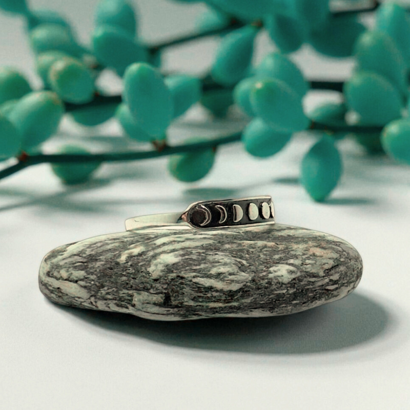 Load image into Gallery viewer, Silver ring with a stone on a white surface with green leaves in the background
