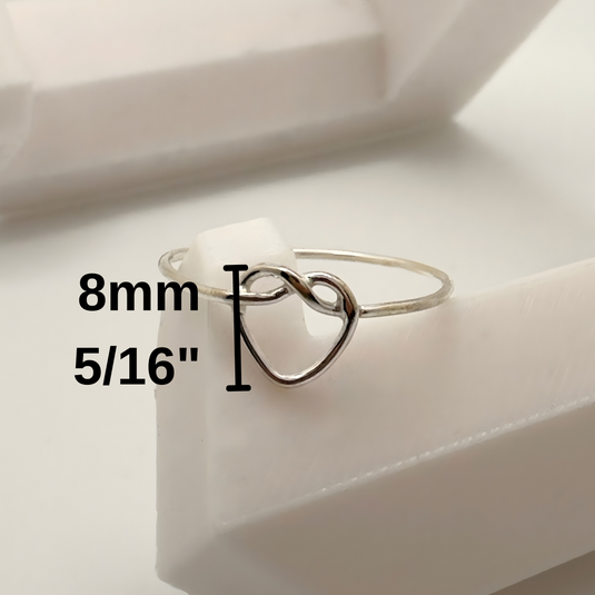 Silver ring with heart design on a white surface, showing size measurement.