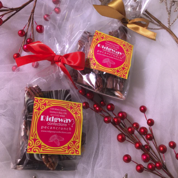 Two packages of Wideway Confections pecan crunch with red ribbons and gold bows on a white background with red berries.
