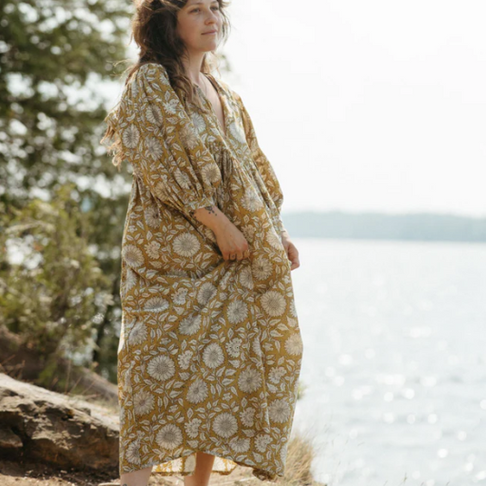Woman in a yellow floral dress standing by a body of water with trees in the background
